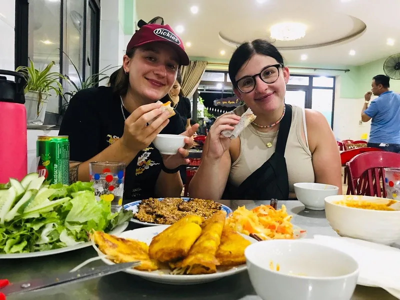 Hai du khách thưởng thức bánh xèo chiên và rau sống tại một quán ăn địa phương trong tour ẩm thực đường phố Hội An.