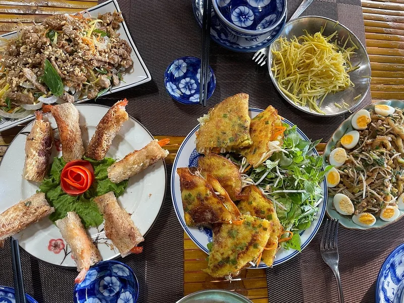 Bàn ăn Việt Nam với chả giò tôm, bánh xèo, rau sống và các món xào bày biện hấp dẫn.