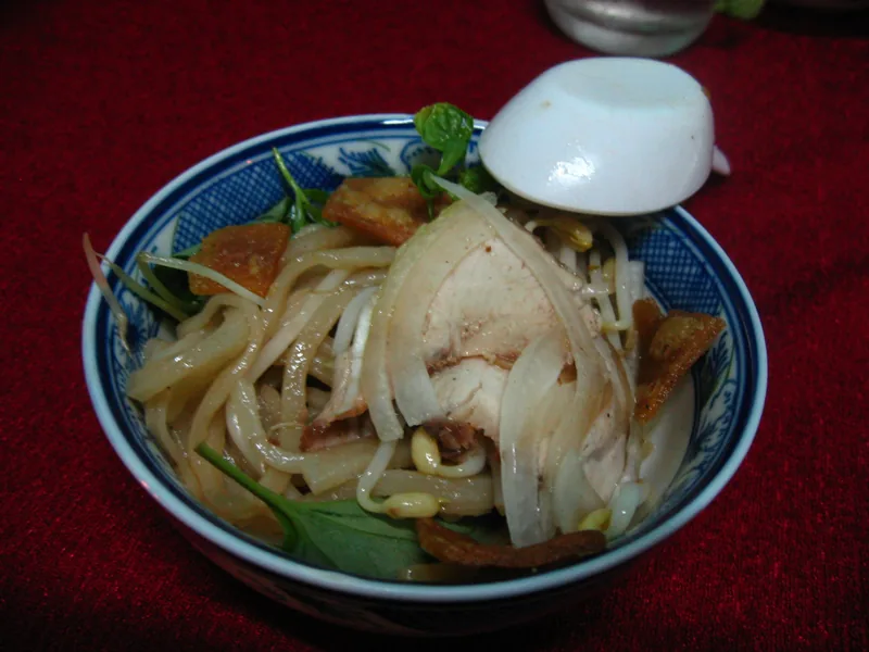 Một tô cao lầu Hội An với sợi mì, thịt heo thái lát, giá đỗ, rau thơm và bánh tráng giòn.