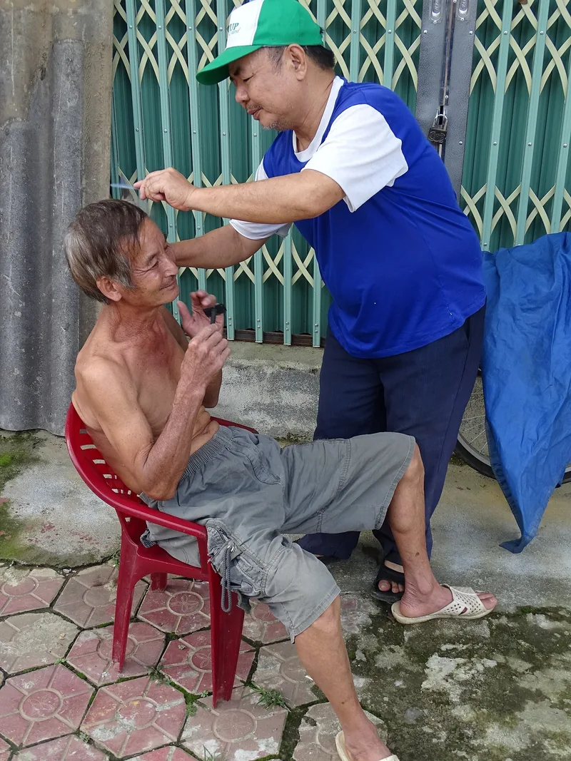 Người thợ cắt tóc vỉa hè đang tỉa lông mày cho một người đàn ông ngồi trên ghế nhựa ở Bắc Hà, Lào Cai.