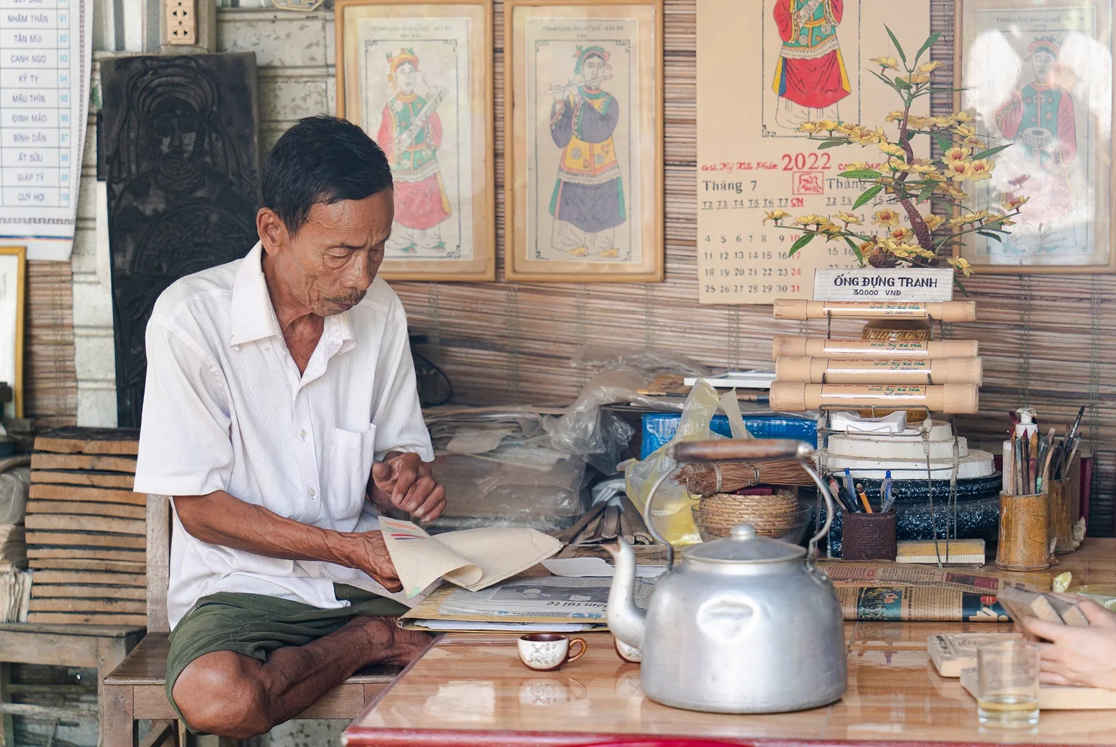 Một người thợ lớn tuổi xem tranh dân gian truyền thống tại bàn làm việc gần Huế.