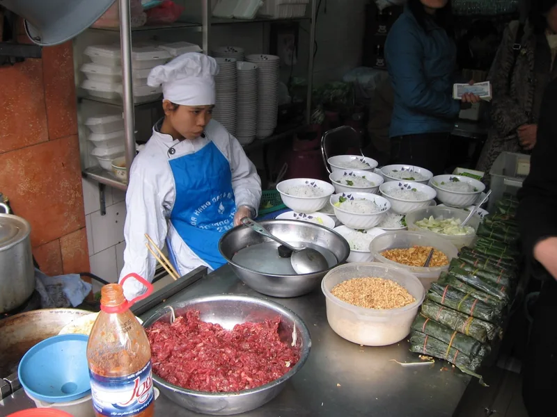 Một người bán hàng ăn trên phố Hà Nội chuẩn bị các bát bún cạnh thịt băm và các loại nguyên liệu ăn kèm.