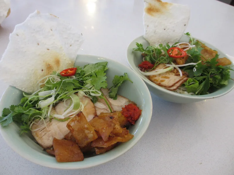 Hai bát mì trộn kiểu Việt Nam với thịt heo thái lát, rau thơm, ớt và bánh tráng nướng trên bàn ở Hội An.